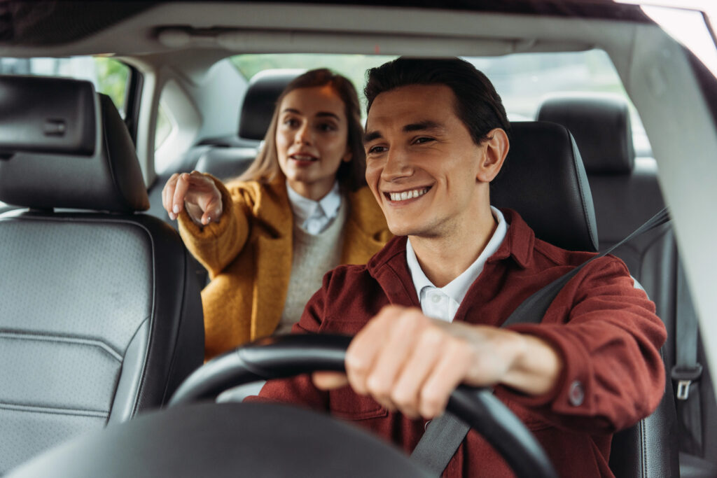Uber driver smilling with a passanger pointing at the road