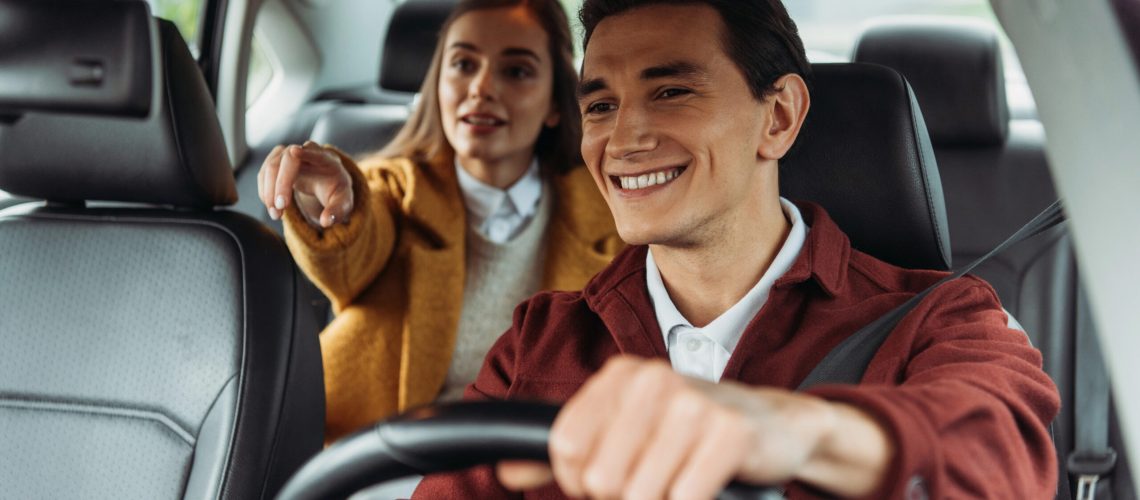 Uber driver smilling with a passanger pointing at the road